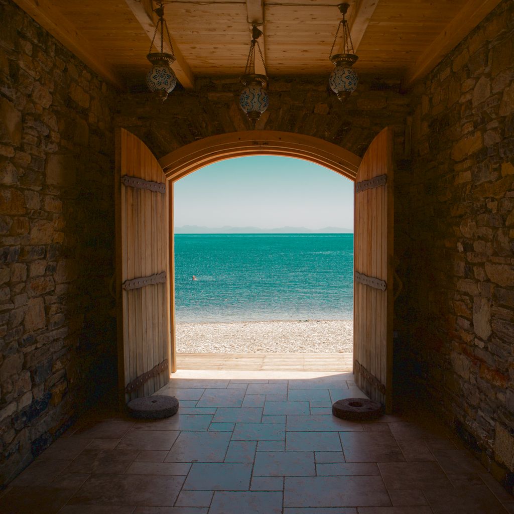 Stunning view of a serene beach and ocean as seen through open wooden doors in a rustic setting.